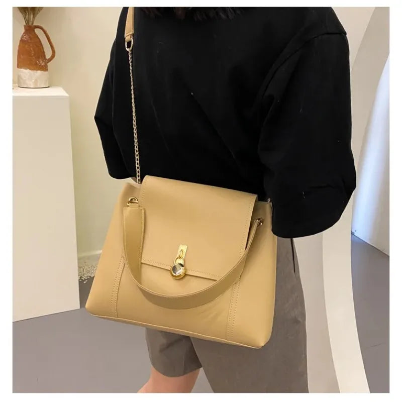Beige shoulder bag with gold clasp and long strap, worn by a person.