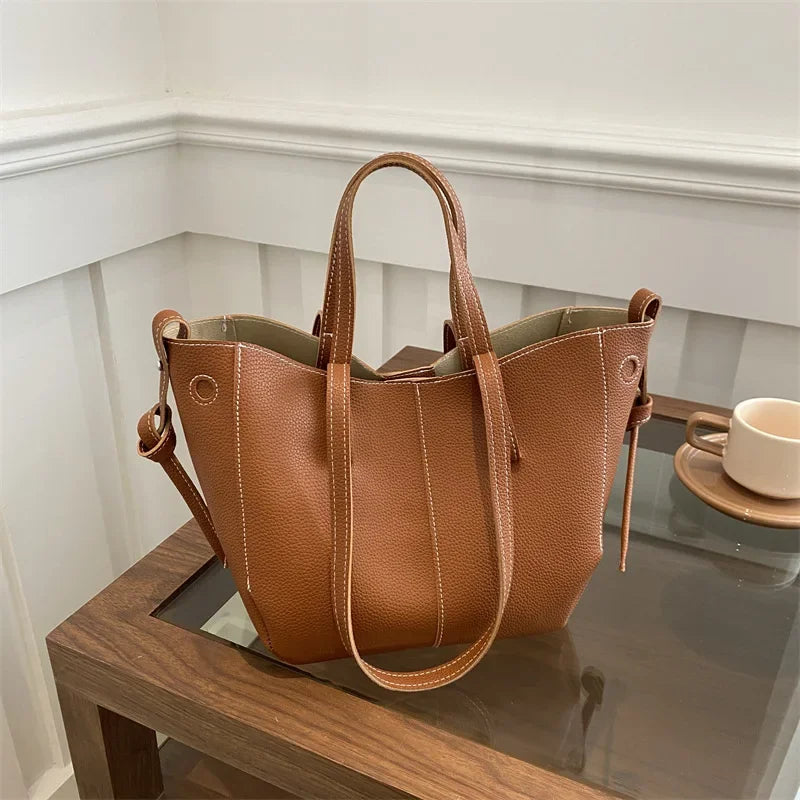Brown leather tote bag with white stitching on a glass table.