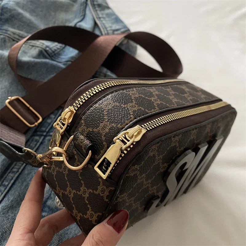 Brown patterned crossbody bag with gold zippers and a wide strap.