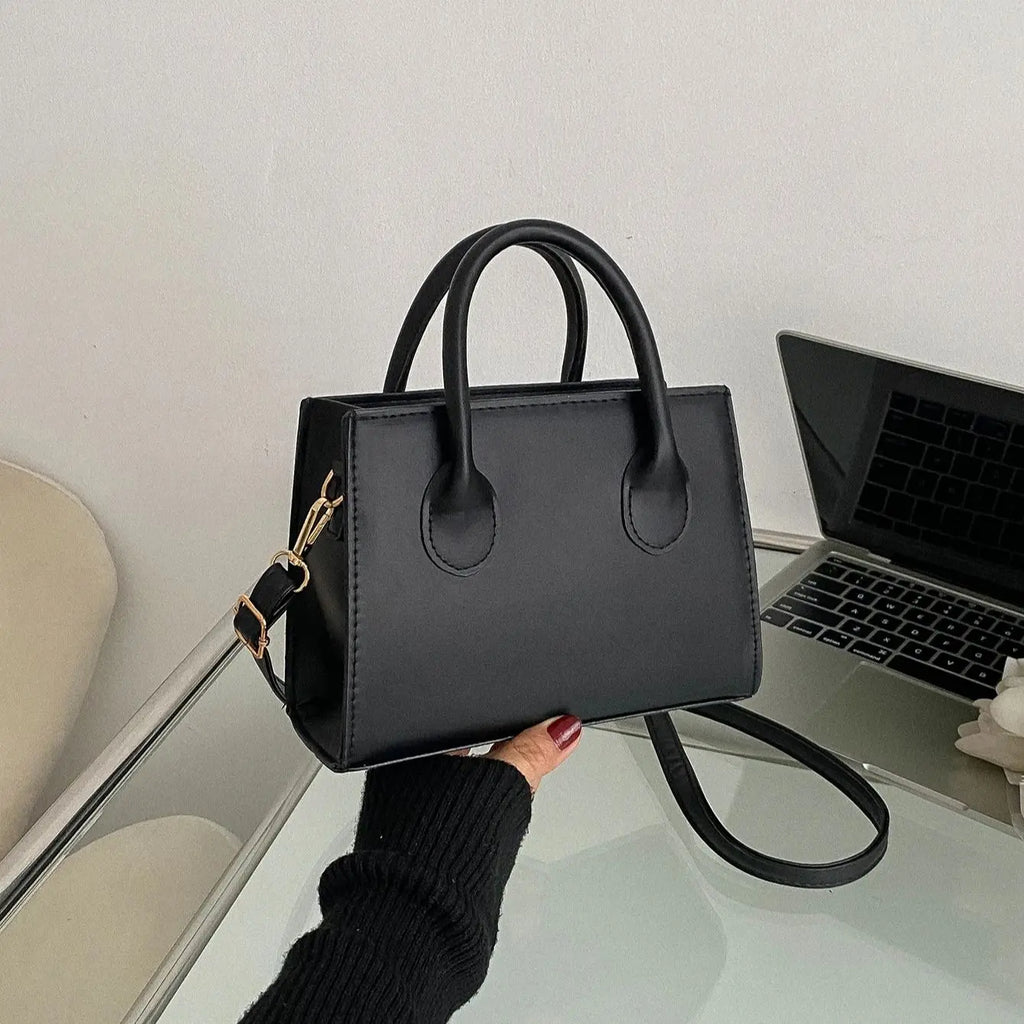 Black leather handbag with gold hardware and dual handles, held in front of a laptop.