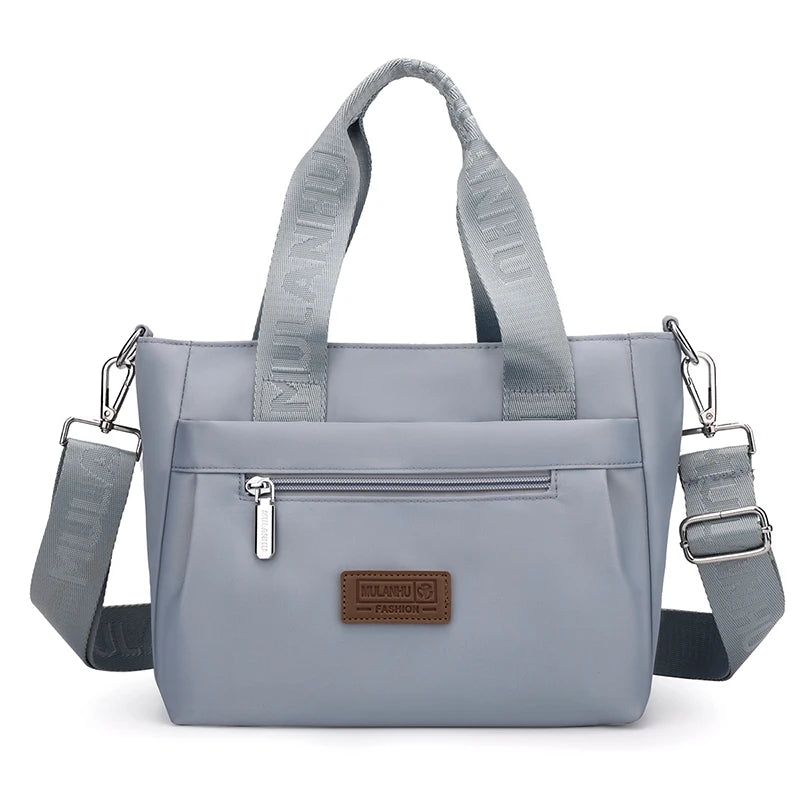 Light blue tote bag with adjustable strap, front pocket, and brand label.