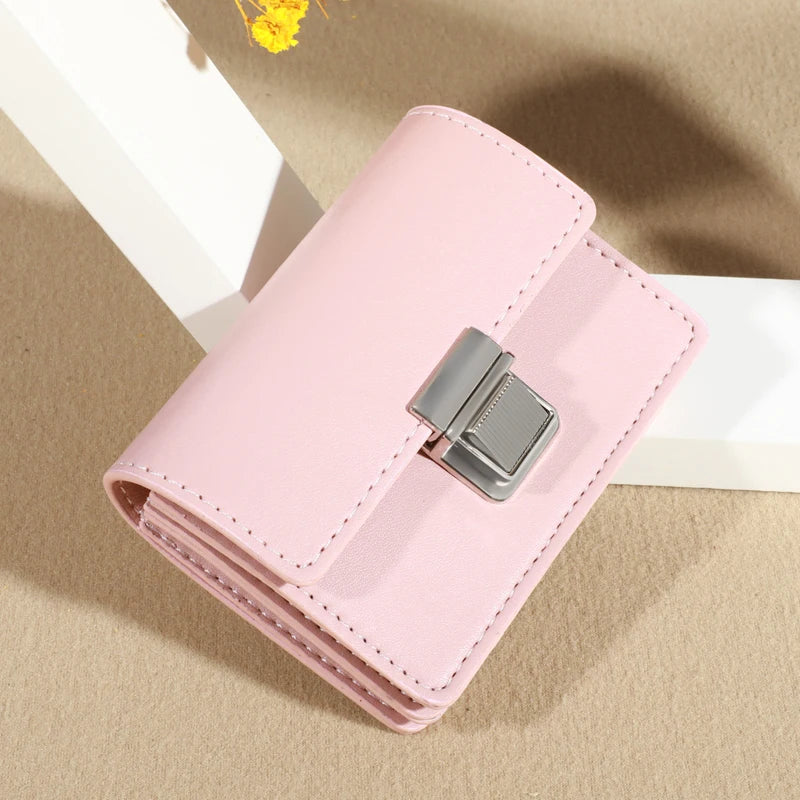 Pink leather wallet with silver clasp, displayed on a textured surface.