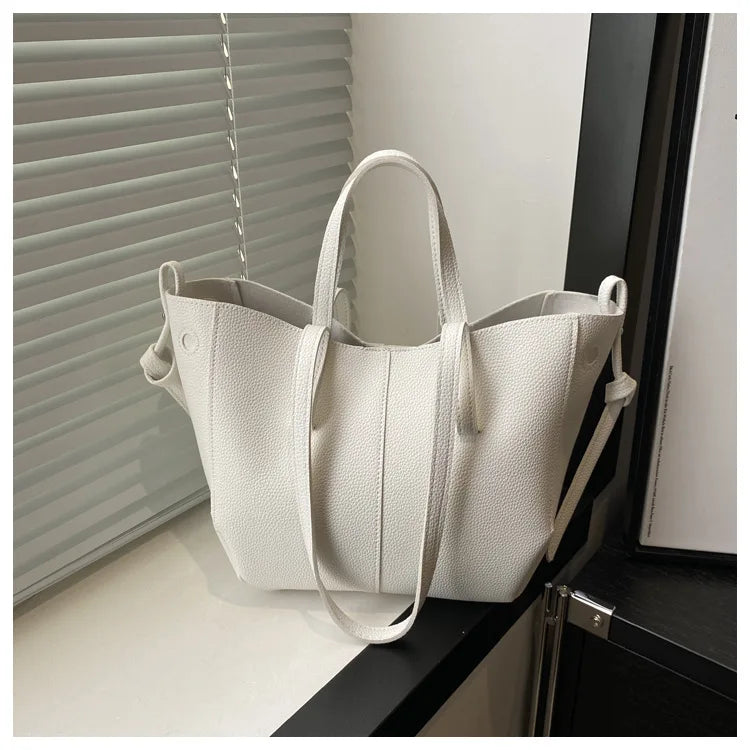 White textured tote bag with dual handles and a shoulder strap, placed on a windowsill.