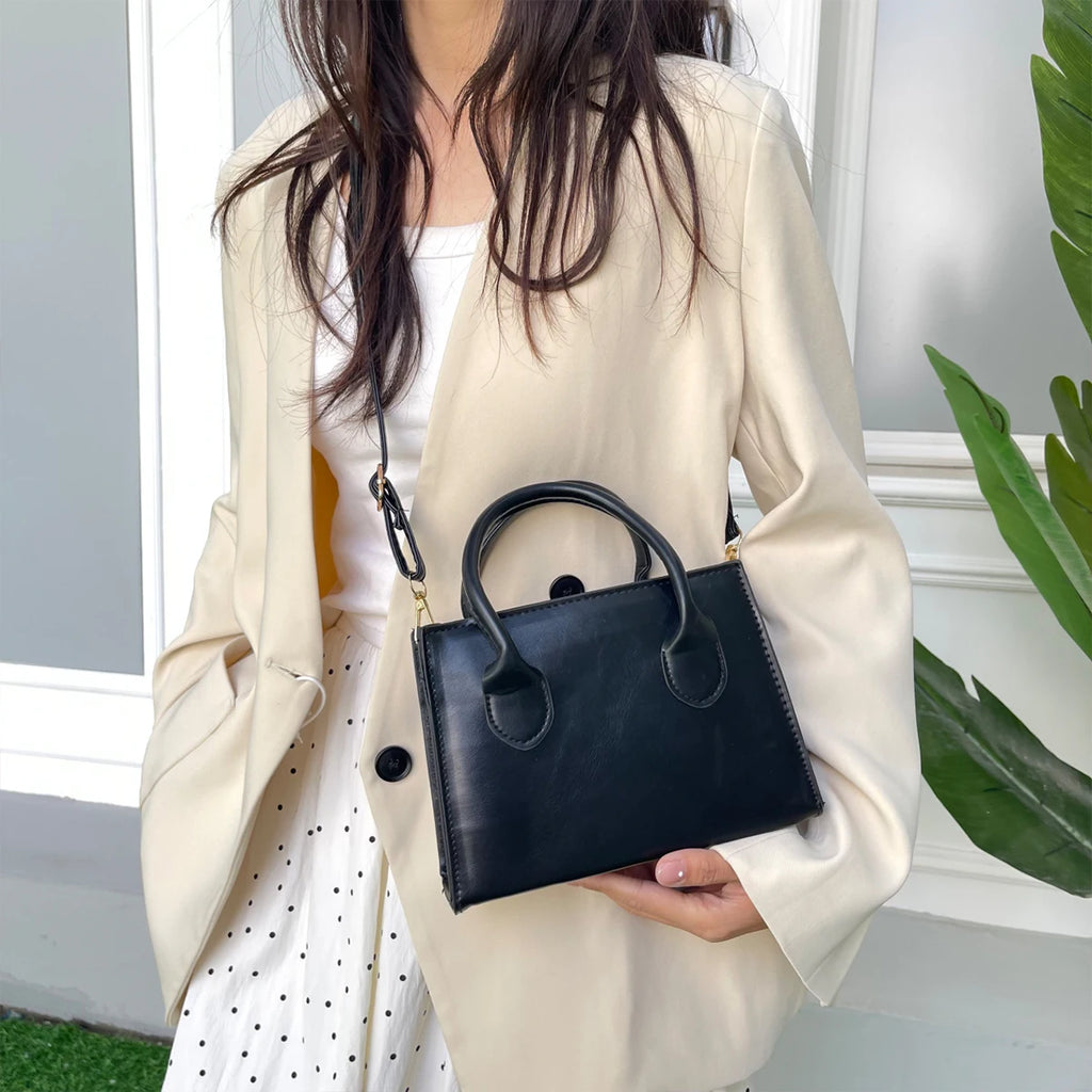 Woman holding a black handbag with top handles and gold accents.