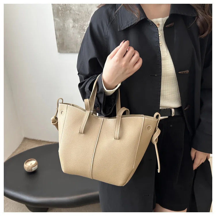 A beige tote bag with two handles, worn by a person in a black jacket.