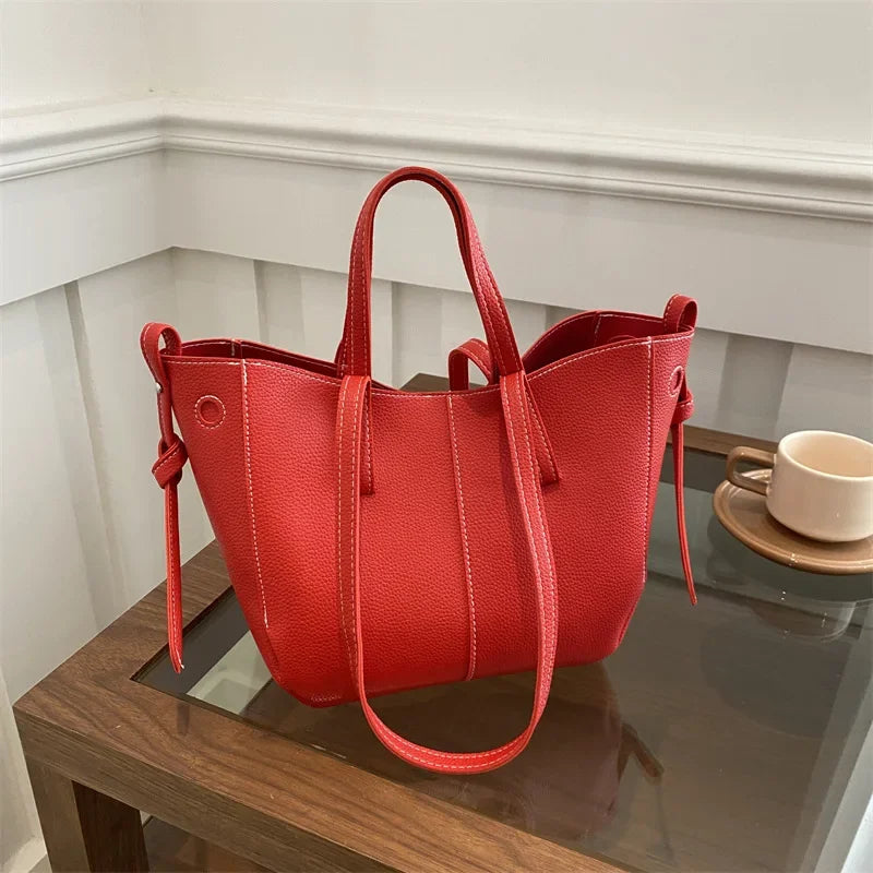 Red textured handbag with white stitching on a glass table.
