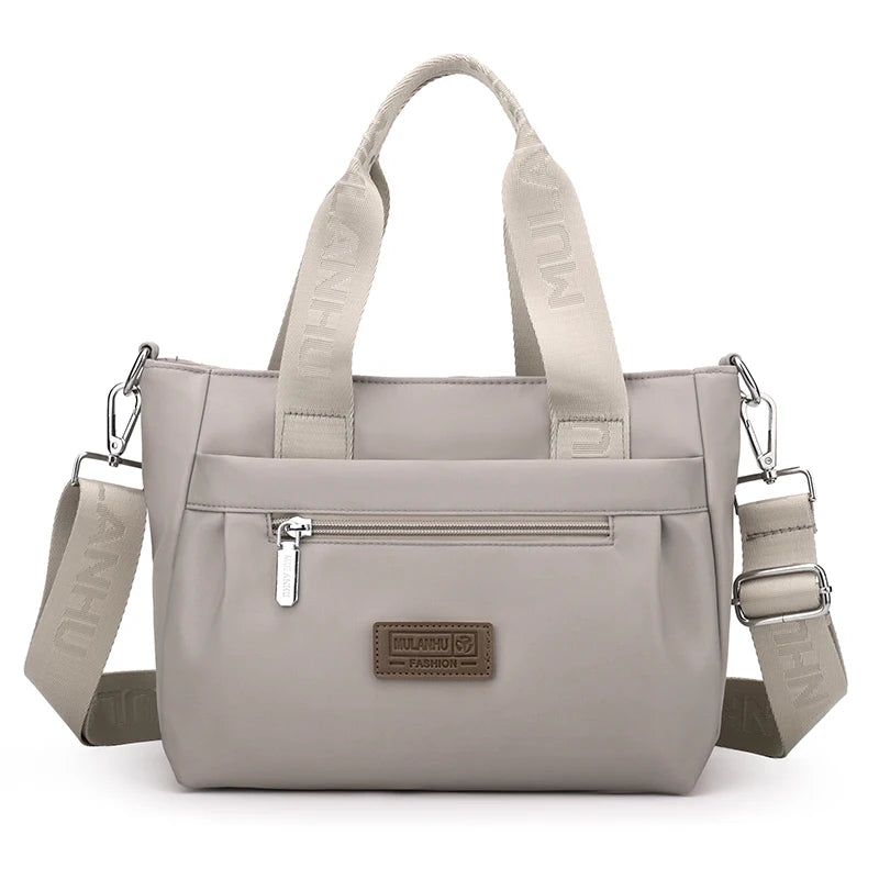 Light gray crossbody bag with top handle, front pocket, and adjustable strap.