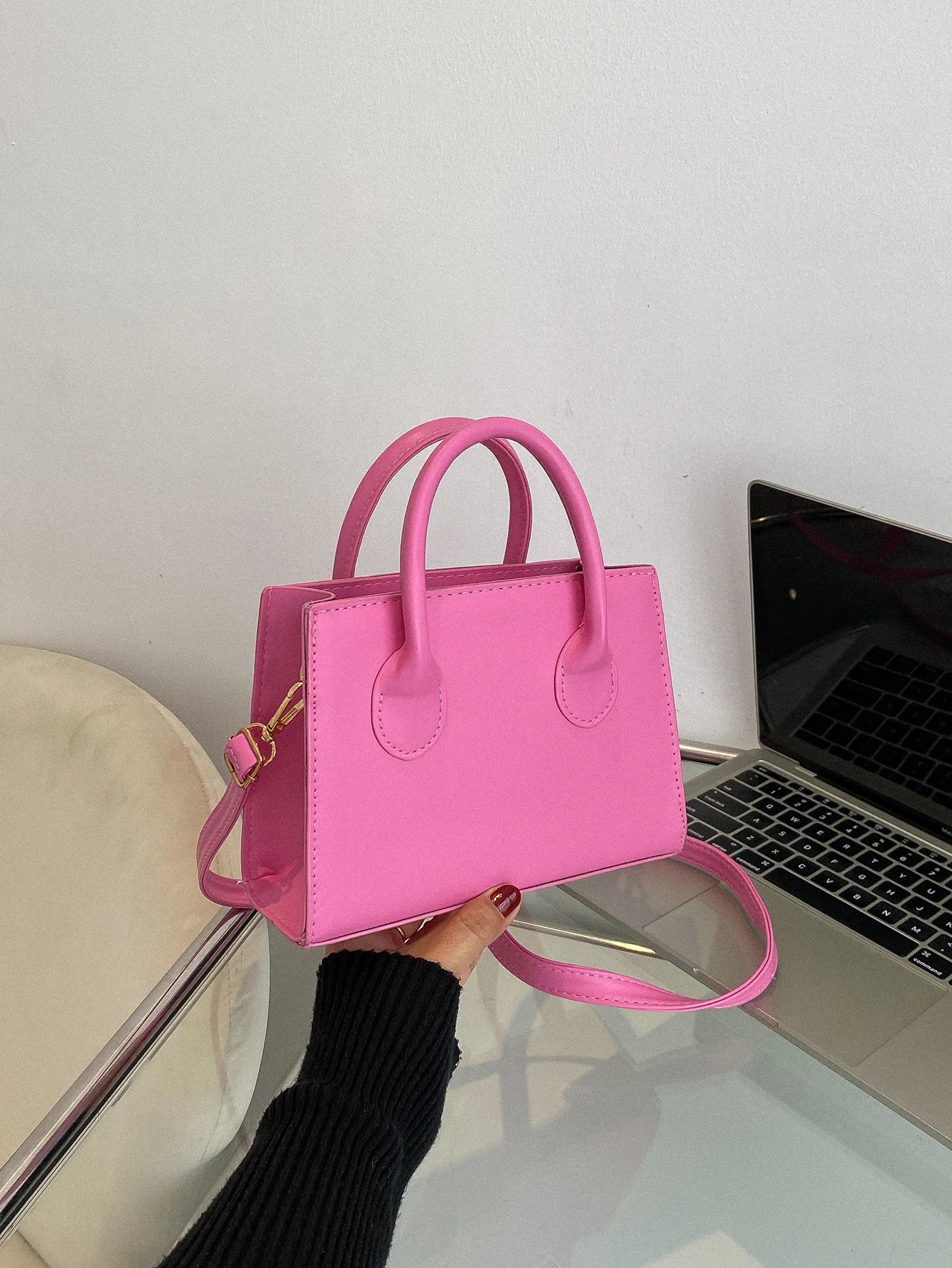 Pink handbag with gold hardware and a detachable strap, held near a laptop.