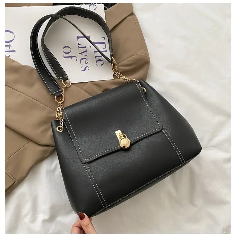 Black leather handbag with gold chain strap and front clasp, styled on a beige jacket.