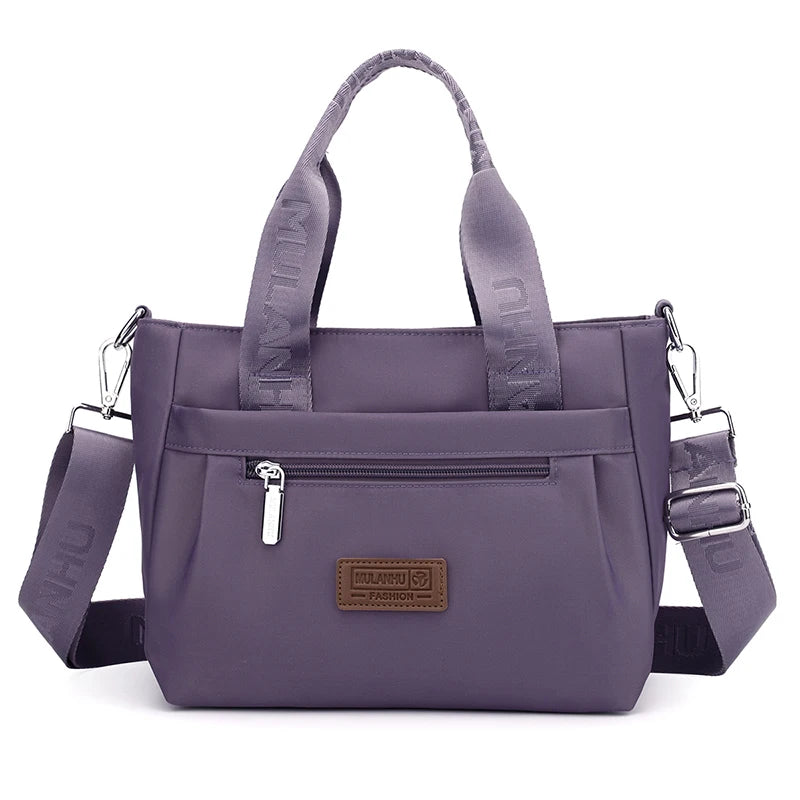 Purple tote bag with adjustable strap, front pocket, and brand label.