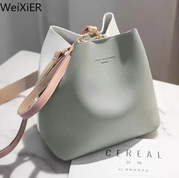 Green and white bucket bag with pink strap and gold hardware on a marble surface.