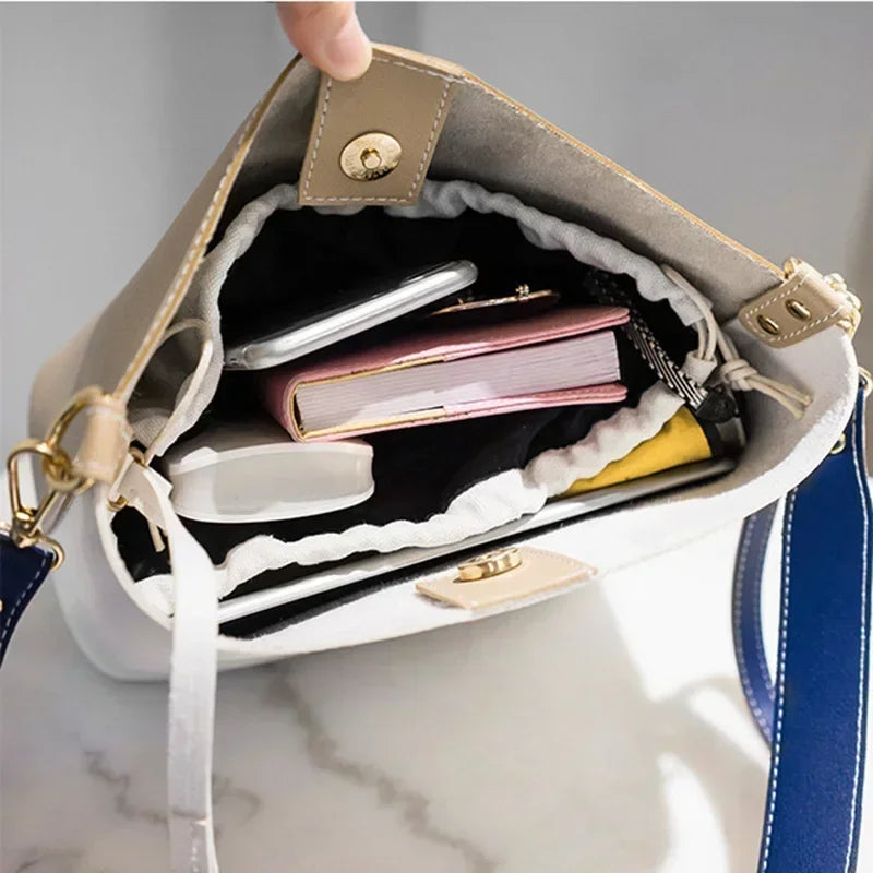 Open beige and white tote bag with gold hardware, filled with books, phone, and accessories.