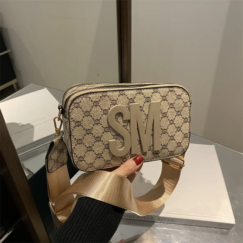 Beige handbag with SM logo and gold strap, held by a hand.