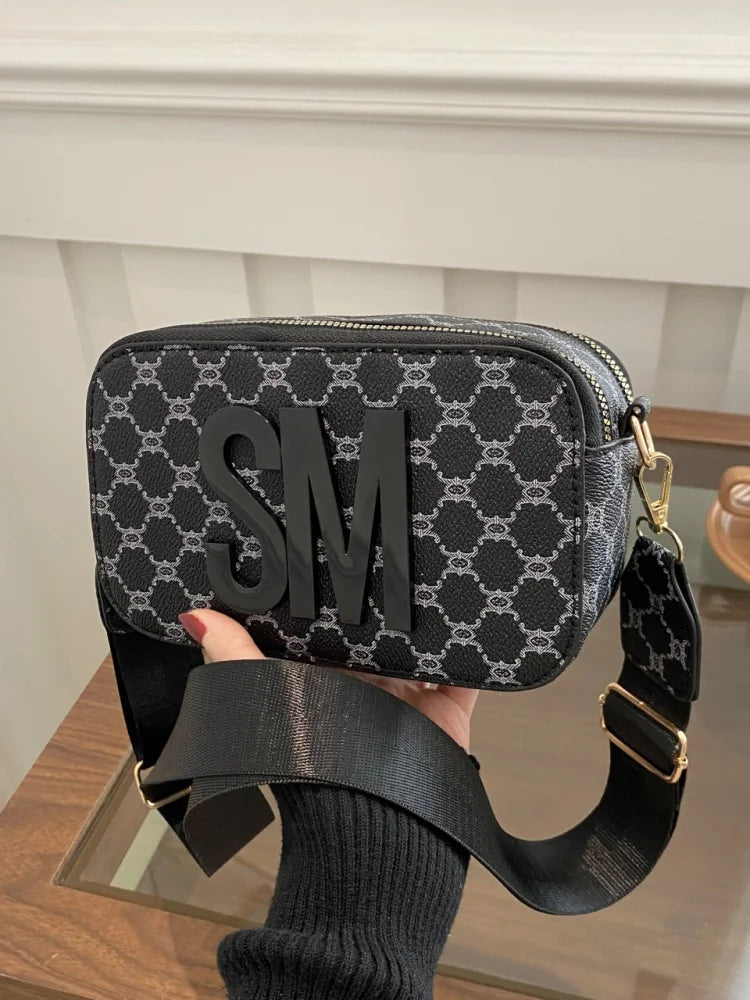 Black and white patterned crossbody bag with SM logo, held by a hand.