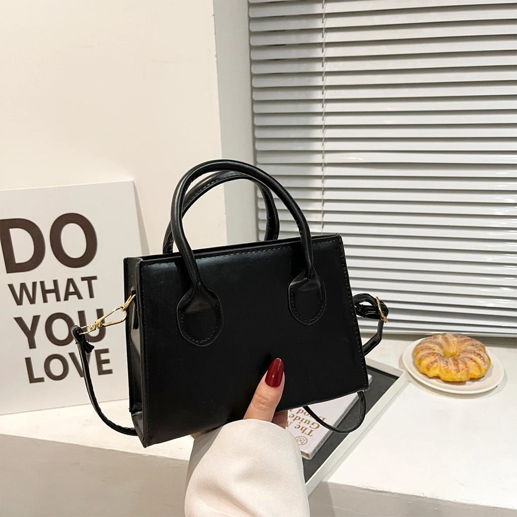 Black handbag with top handles and gold chain accents, held in hand.