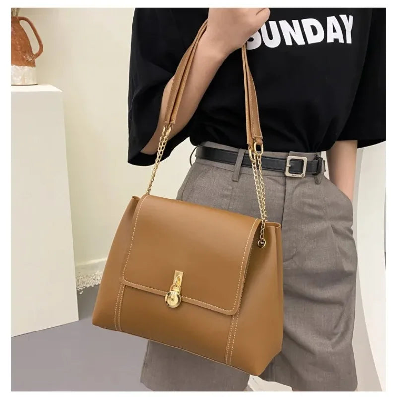 Woman holding a brown leather handbag with gold hardware and chain strap.