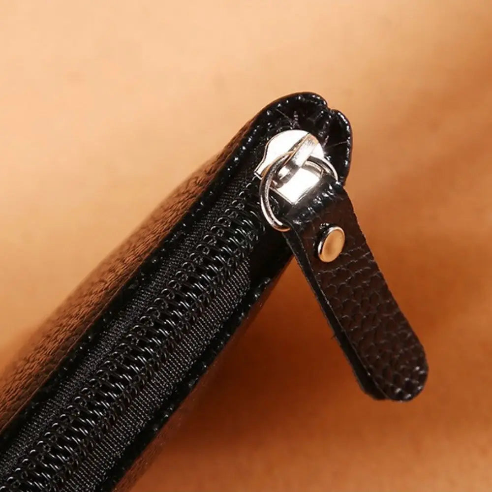Black textured wallet with silver zipper and pull tab on a warm background.
