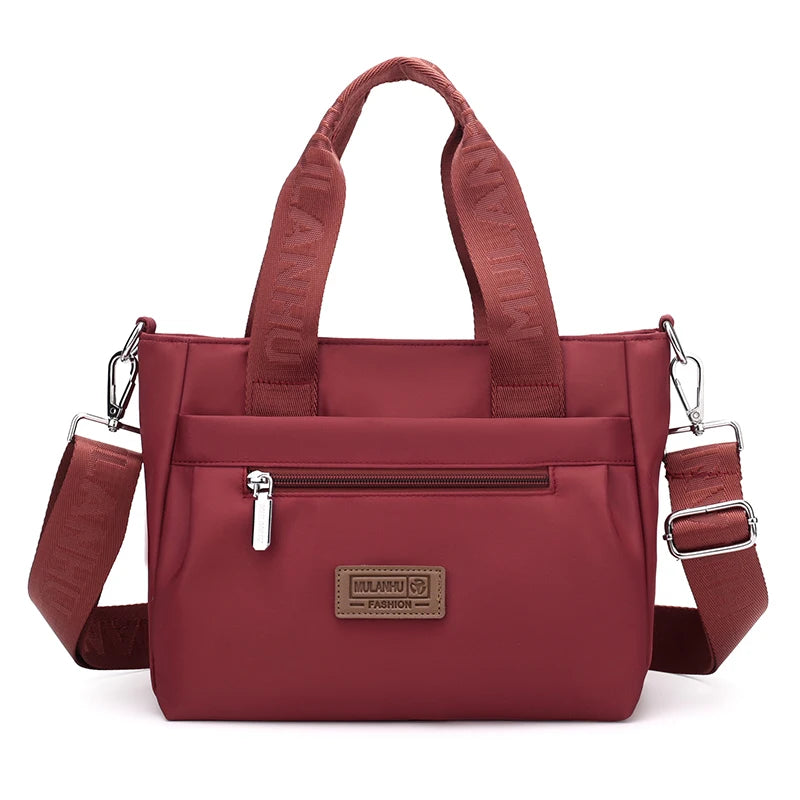 Red tote bag with adjustable strap, front pocket, and brand label.