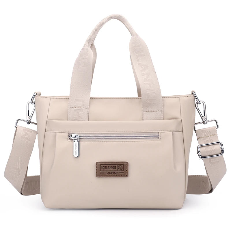 Beige handbag with top handle and adjustable shoulder strap, featuring front pocket and brand label.