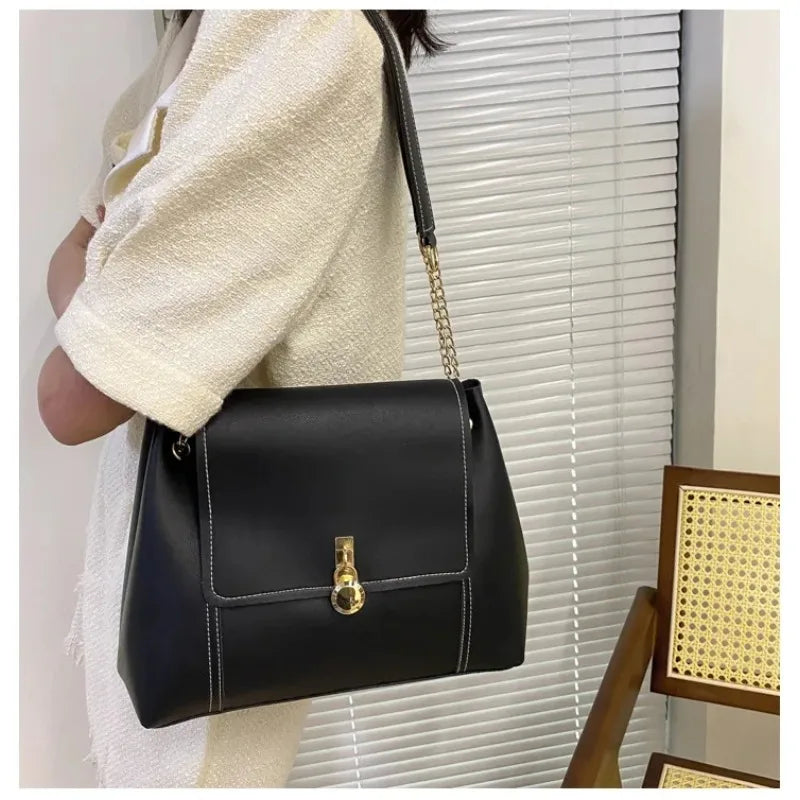Black leather shoulder bag with gold clasp and stitching, worn by a person.
