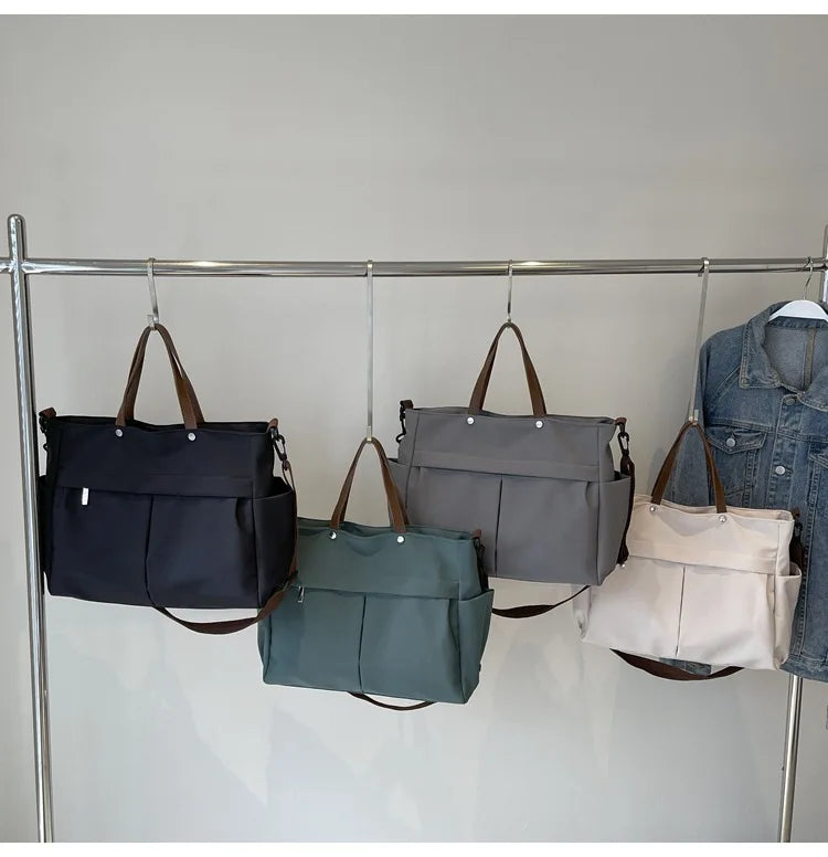 Four tote bags in black, gray, and blue hanging on a metal rack.